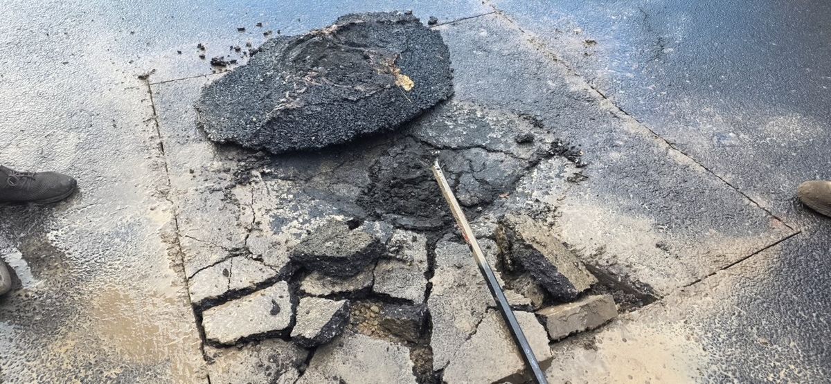 Broken asphalt slabs cut out and stacked beside an open pavement repair area.
