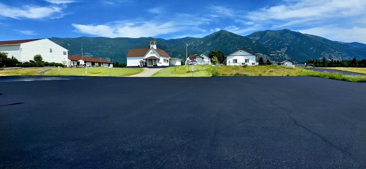 Wide freshly coated parking area in front of a white building with a mountain ridge behind.