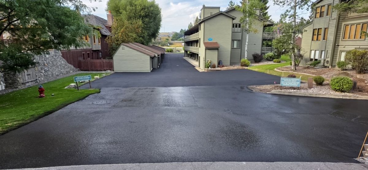 Freshly paved asphalt access drive running between multiple residential buildings and a detached garage row.