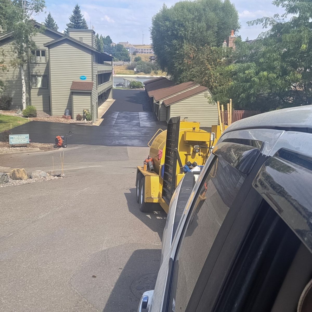 Yellow compact loader parked on an asphalt access drive beside multi-story residential buildings.