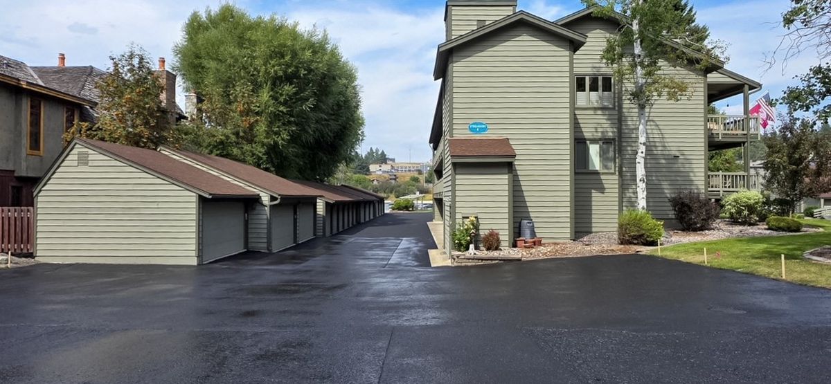 New asphalt drive lane running alongside a row of open garage bays and a multi-story building.