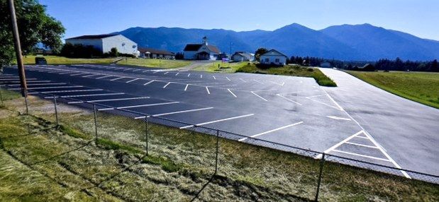 Finished striped asphalt parking lot with open ground and a mountain ridge in the background.