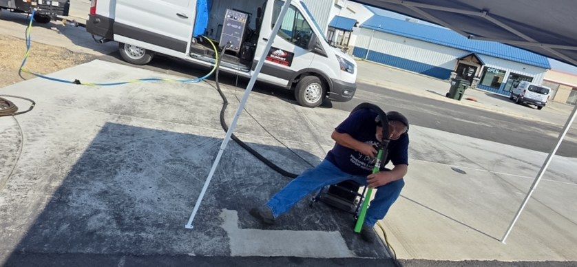 Worker kneeling with a hose line on a concrete forecourt next to a white service van.