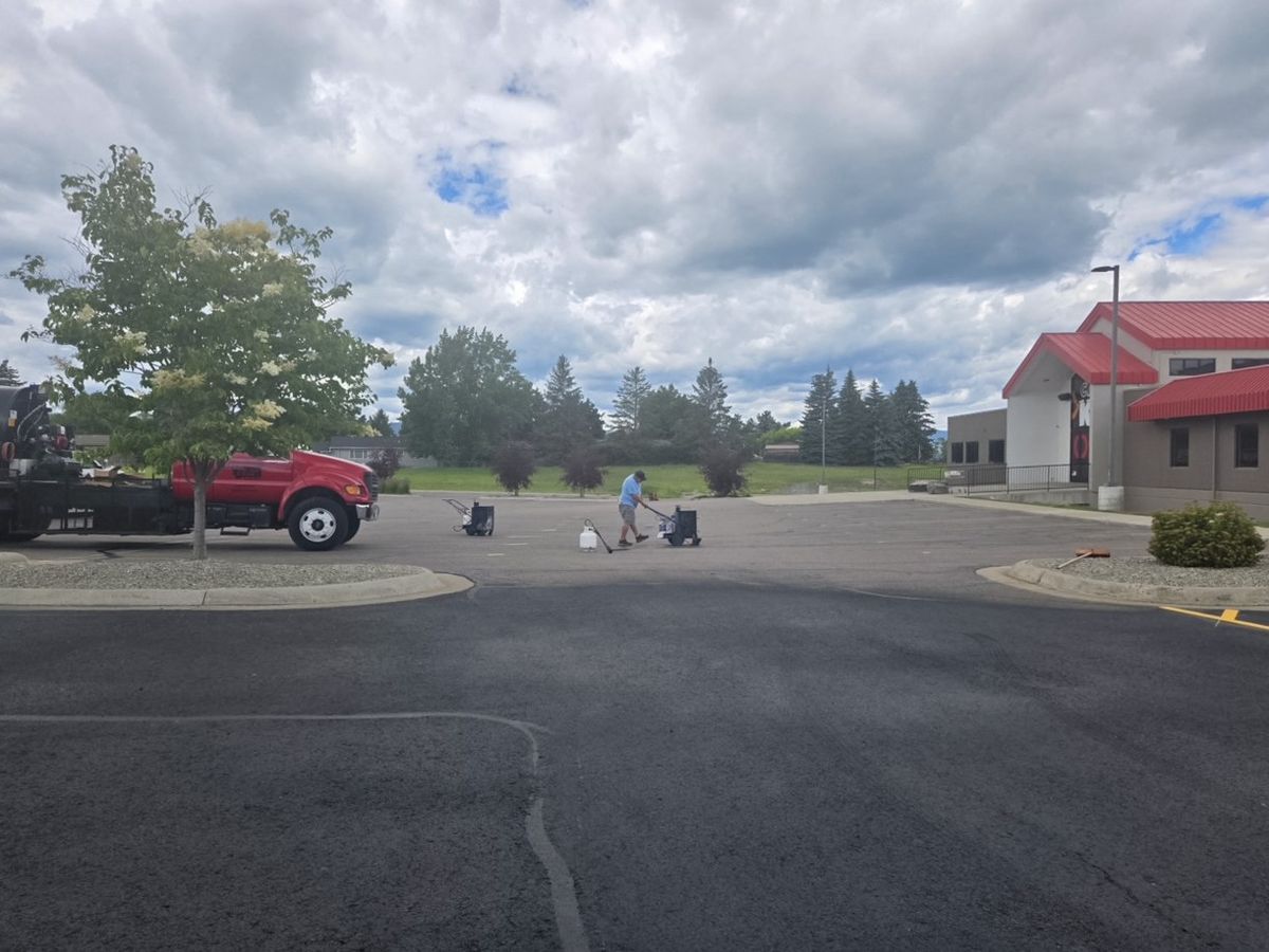 Crew members and equipment staged on an asphalt parking lot in front of a red-roofed building.