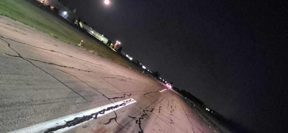 Treated crack lines running across a pavement surface at night under work lighting.