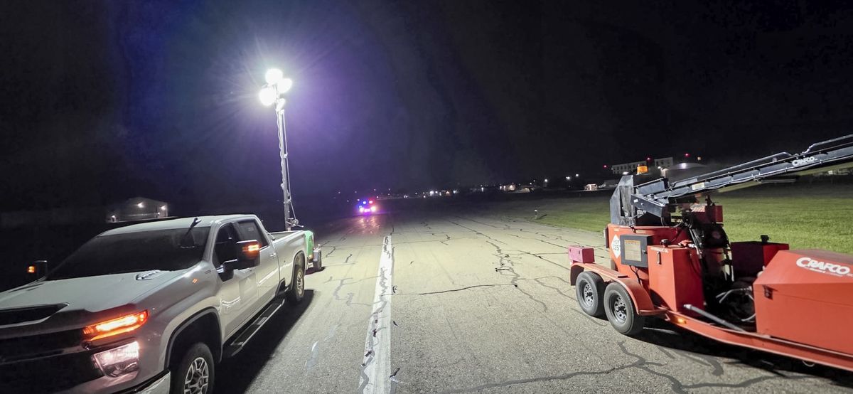 Portable light tower illuminating a paved work area at night beside a truck and equipment.
