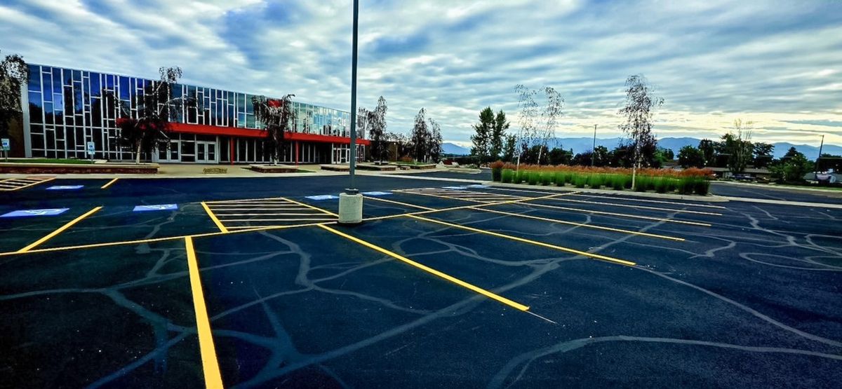 Freshly sealed and yellow-striped parking lot in front of a glass-fronted office building.