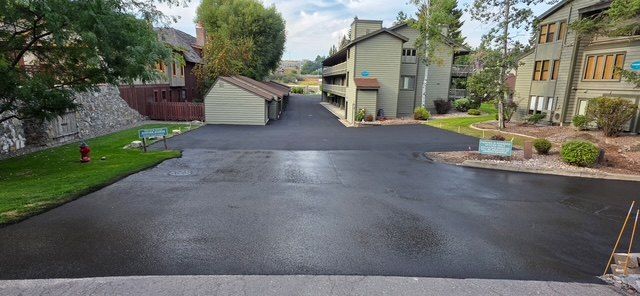 Freshly paved asphalt access drive running between multiple residential buildings and a detached garage row.
