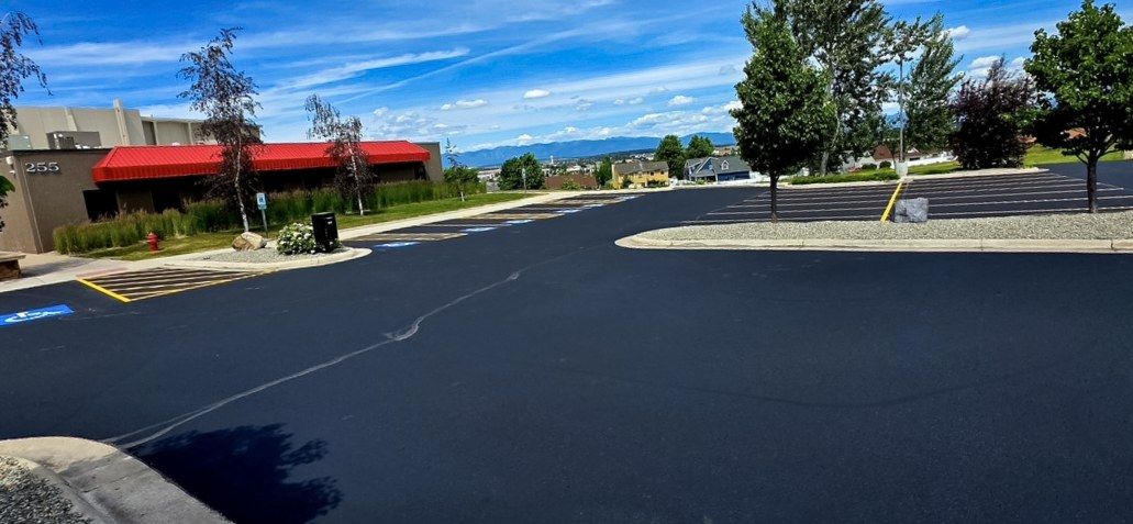 Freshly coated asphalt parking area and drive aisle along a retail building with a red awning.