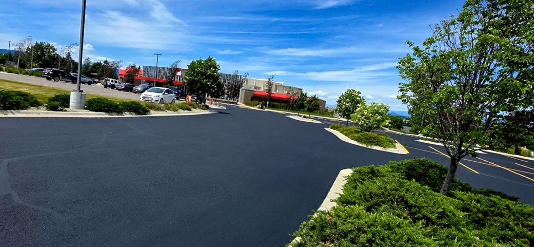 Freshly coated drive aisle running past curbed landscape islands in a commercial parking lot.