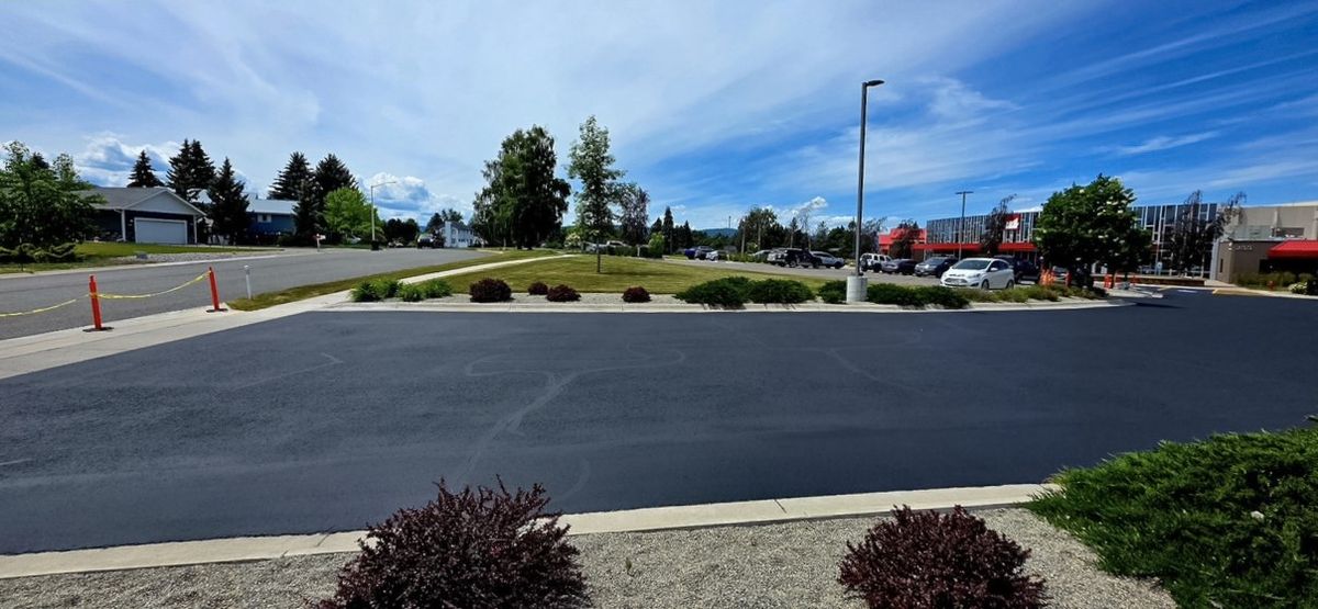 Freshly coated asphalt aisle running along a curb line and planting beds at a commercial property.