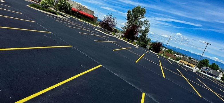 Yellow parking stall lines painted across a freshly sealed black asphalt commercial lot.