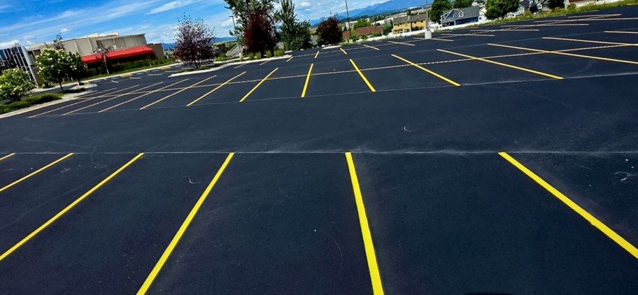 Completed yellow parking stall layout on a black asphalt lot in front of a commercial building.