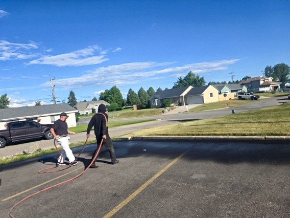 Two crew members applying sealer by hose beside a yellow painted centerline on a residential street.