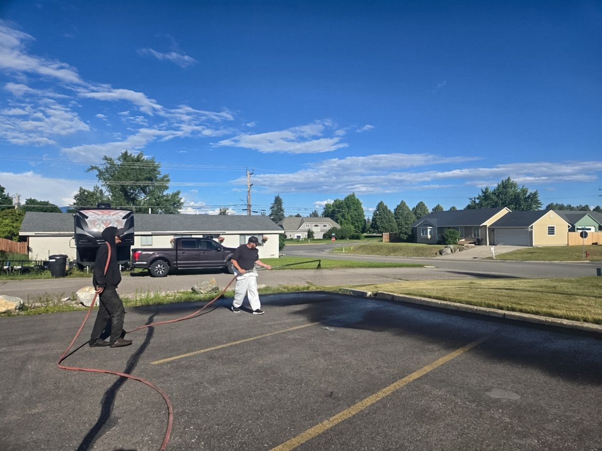 Wide view of two workers applying sealer across a residential street under a clear blue sky.