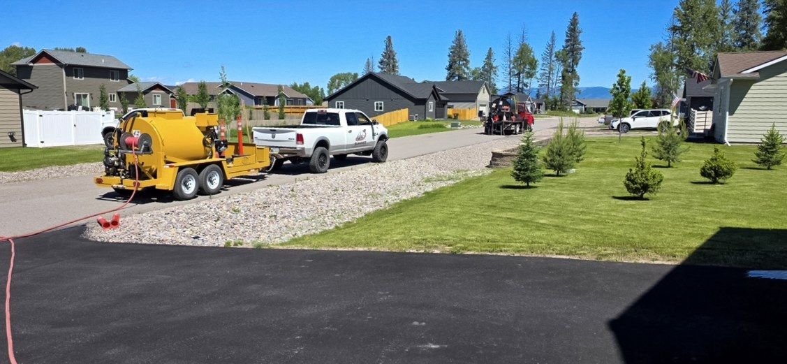 Yellow sealer trailer and white service truck parked on a neighborhood driveway.
