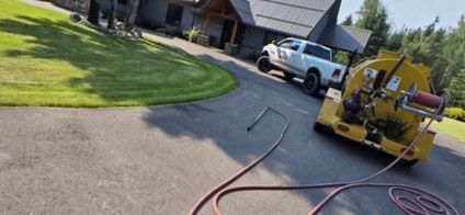 Sealer application unit and pickup truck on a residential driveway with hoses laid out.