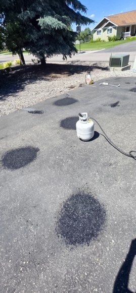 Dark treated spots on a gray residential driveway with a small tank and hose nearby.