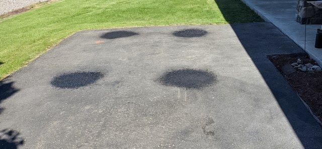 Dark treated spots on a light-colored concrete drive apron beside a lawn and walkway.