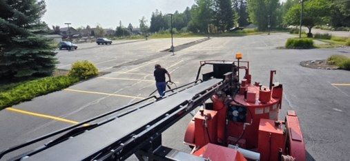 Red ride-on line striping machine applying stall lines on a black asphalt parking lot.