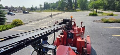 View over the boom of a red line striping machine working across an asphalt parking lot.
