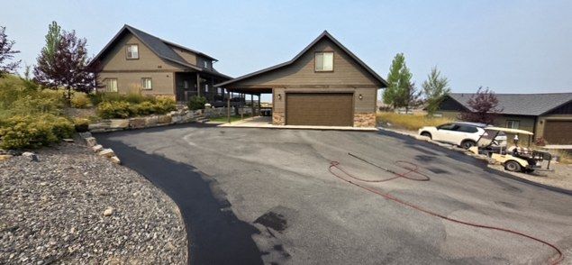 Finished asphalt driveway and apron curving in front of a building with attached garage doors.