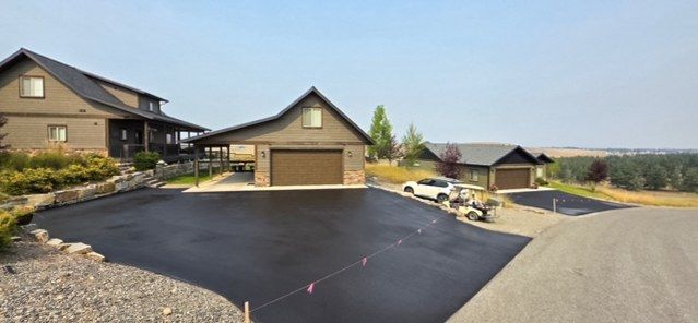 Black asphalt apron in front of attached garage doors, with the pavement edge meeting a grass lawn.