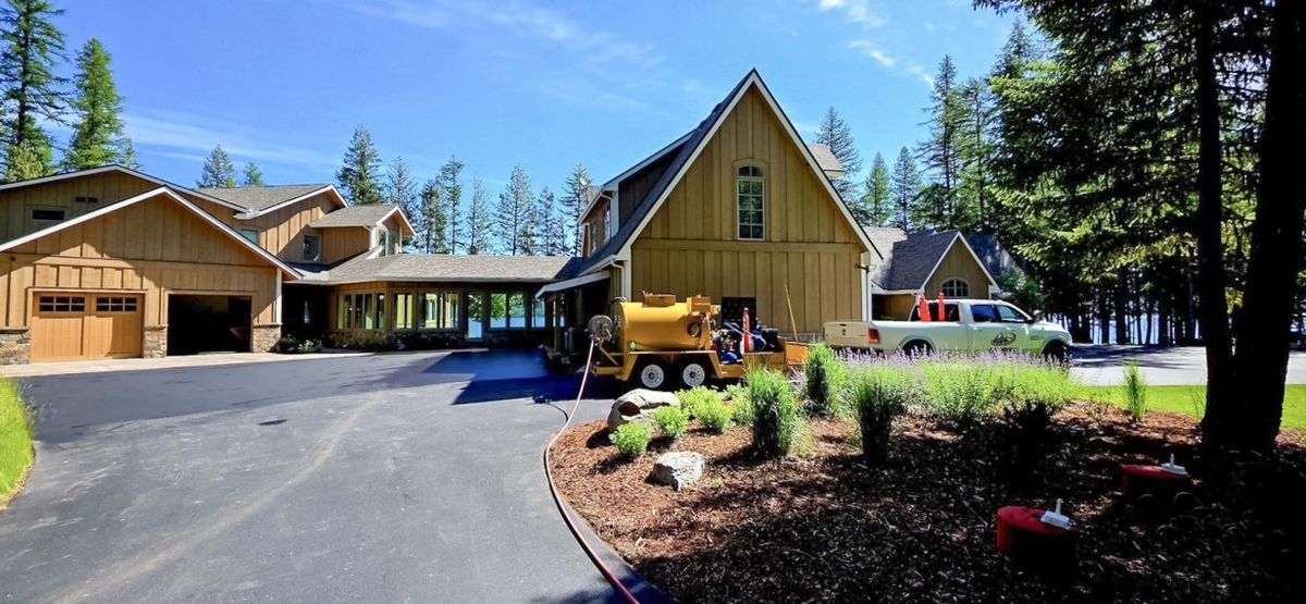 Sealcoating equipment staged at the top of a long residential driveway beside a house.